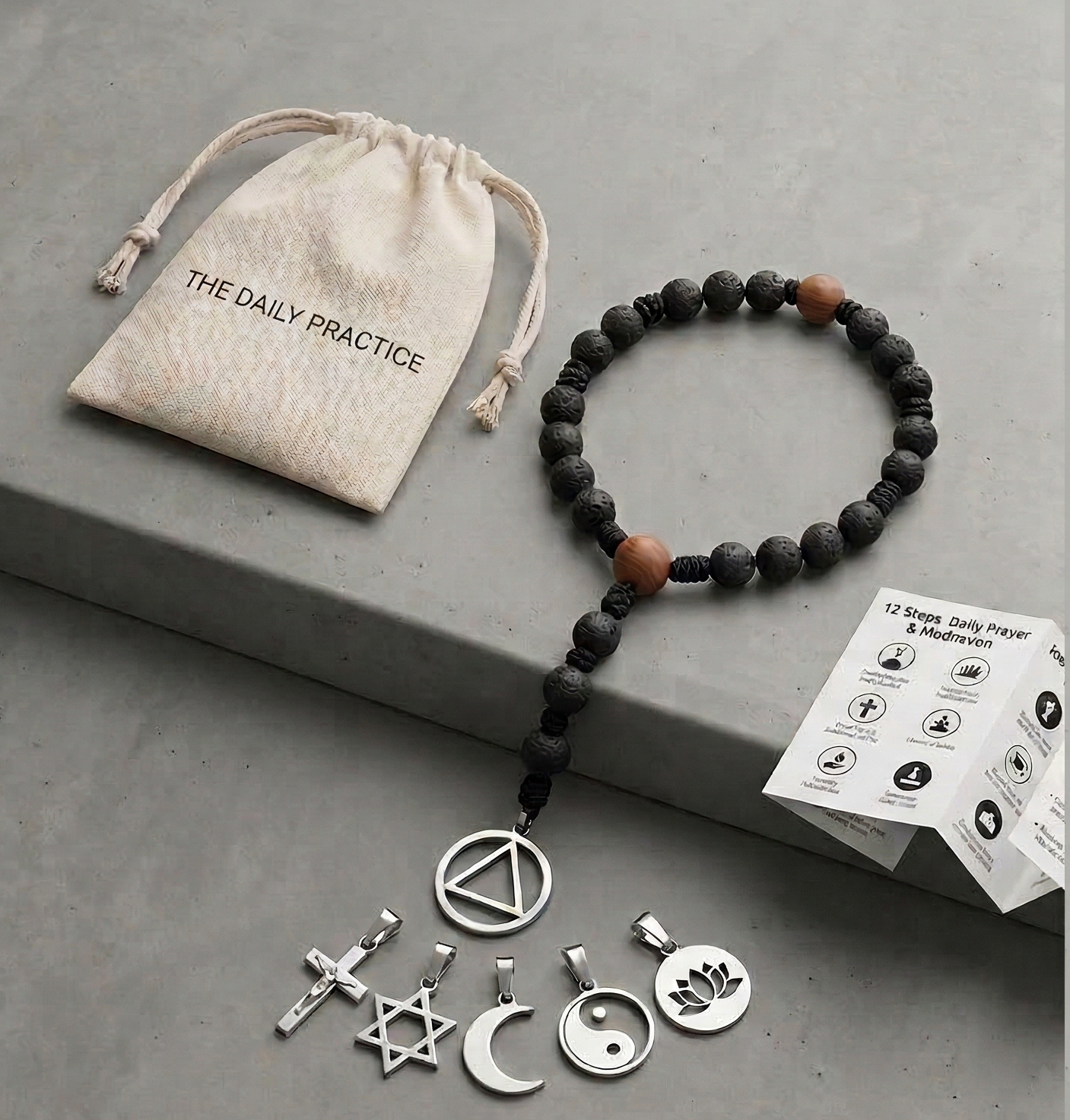 The 12-Step Rosary: a black lava-bead rosary with a small linen pouch labelled 'The Daily Practice', shown alongside interchangeable pendants — cross, Star of David, crescent moon, AA circle and triangle, yin-yang, lotus.